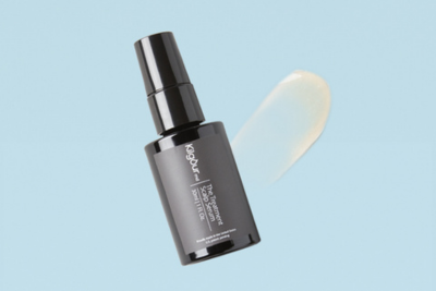 Angled view of KilgourMD hair serum bottle showcasing a pale yellow serum smear on a light blue background