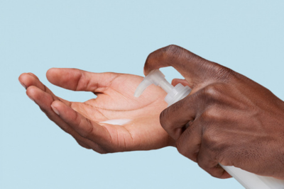 Dark-skinned hands dispensing foam from a white pump bottle against a pale blue background