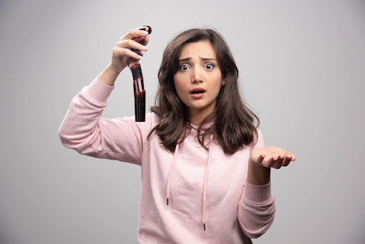 Young woman in pink hoodie holding a hairbrush with a clump of shed hair, looking surprised