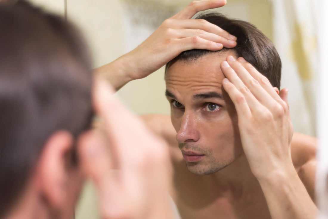 Man examining his hairline in a bathroom mirror
