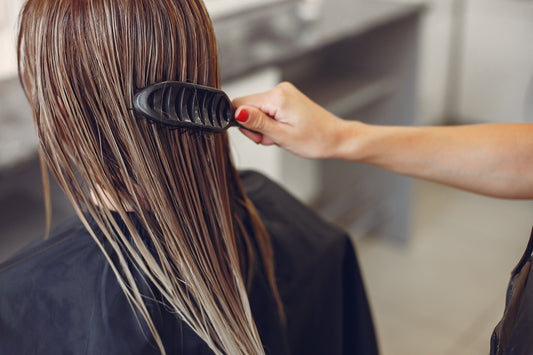 Salon stylist brushing wet long hair of a seated client