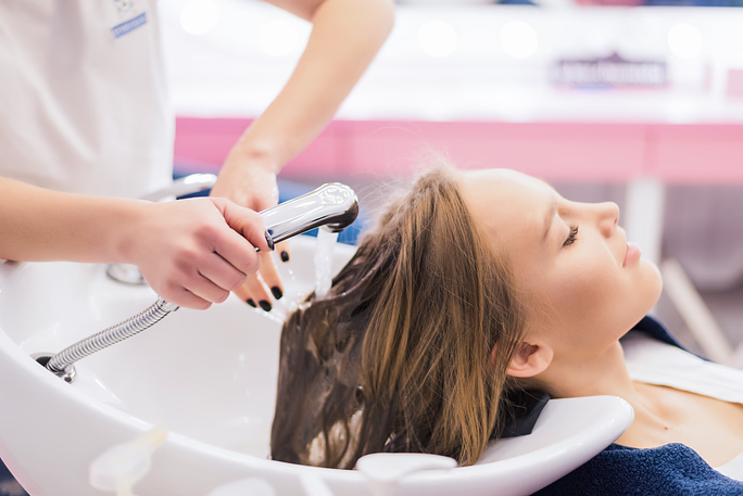 Woman reclining with eyes closed as a stylist rinses her hair in a salon shampoo basin
