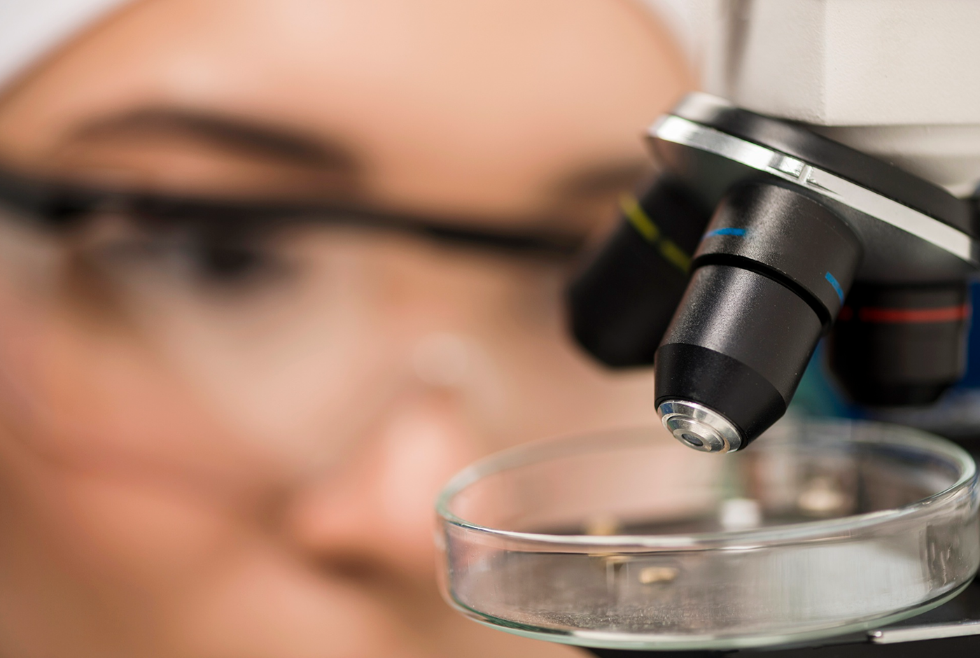 Microscope examining a laboratory sample with a researcher blurred in the background