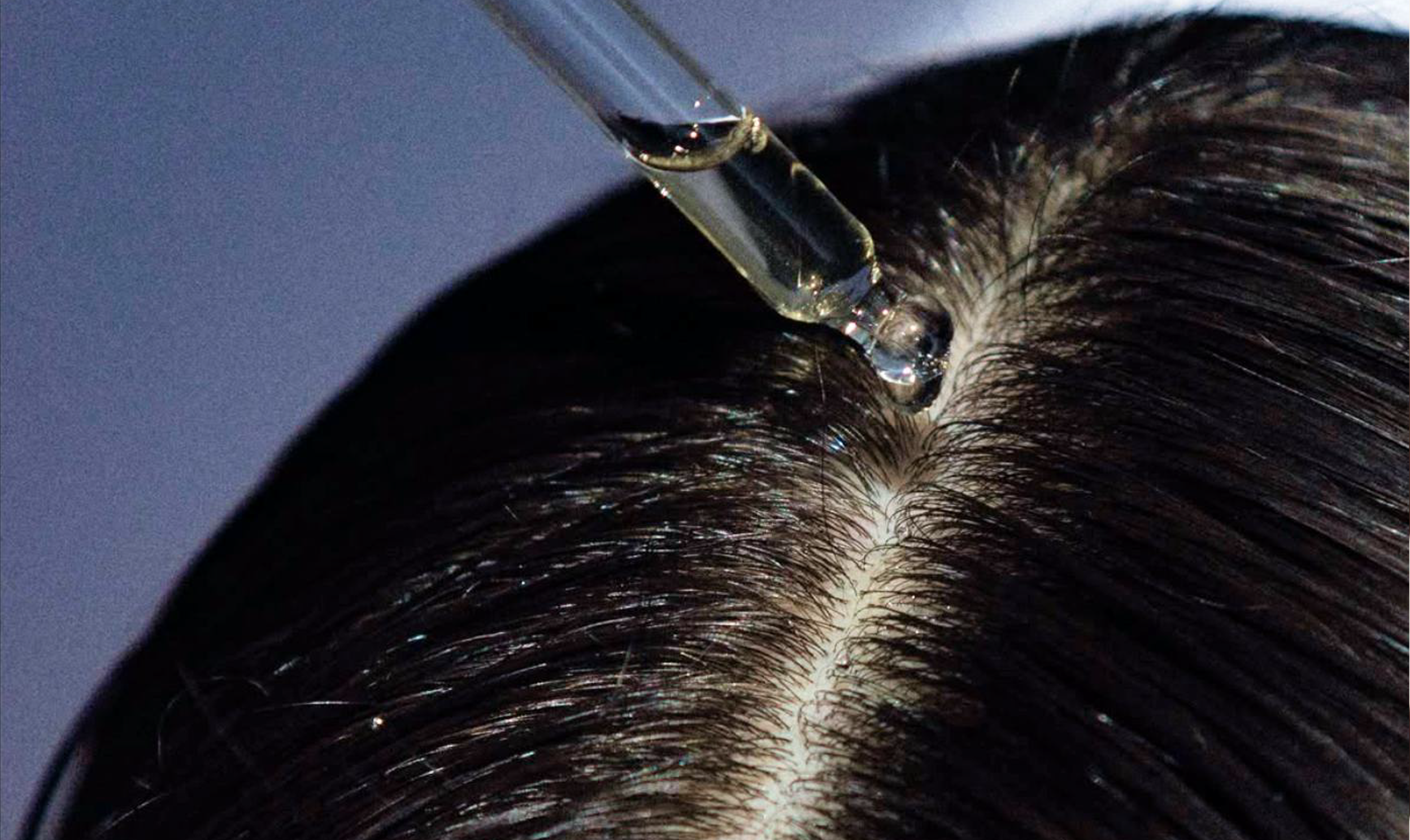 Applicator applying topical treatment to a parted scalp in close up