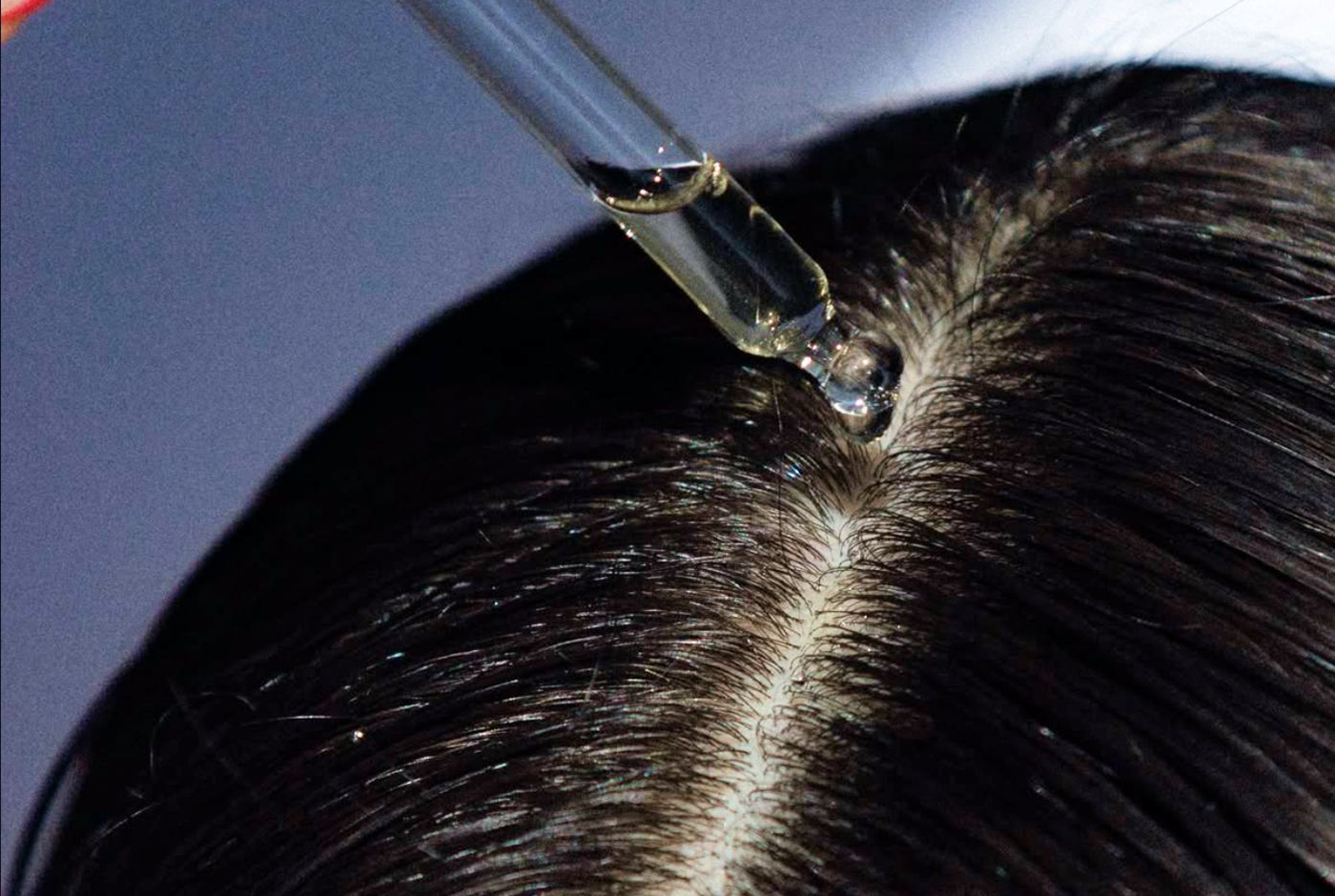 Dropper applying a topical hair serum to a parted scalp