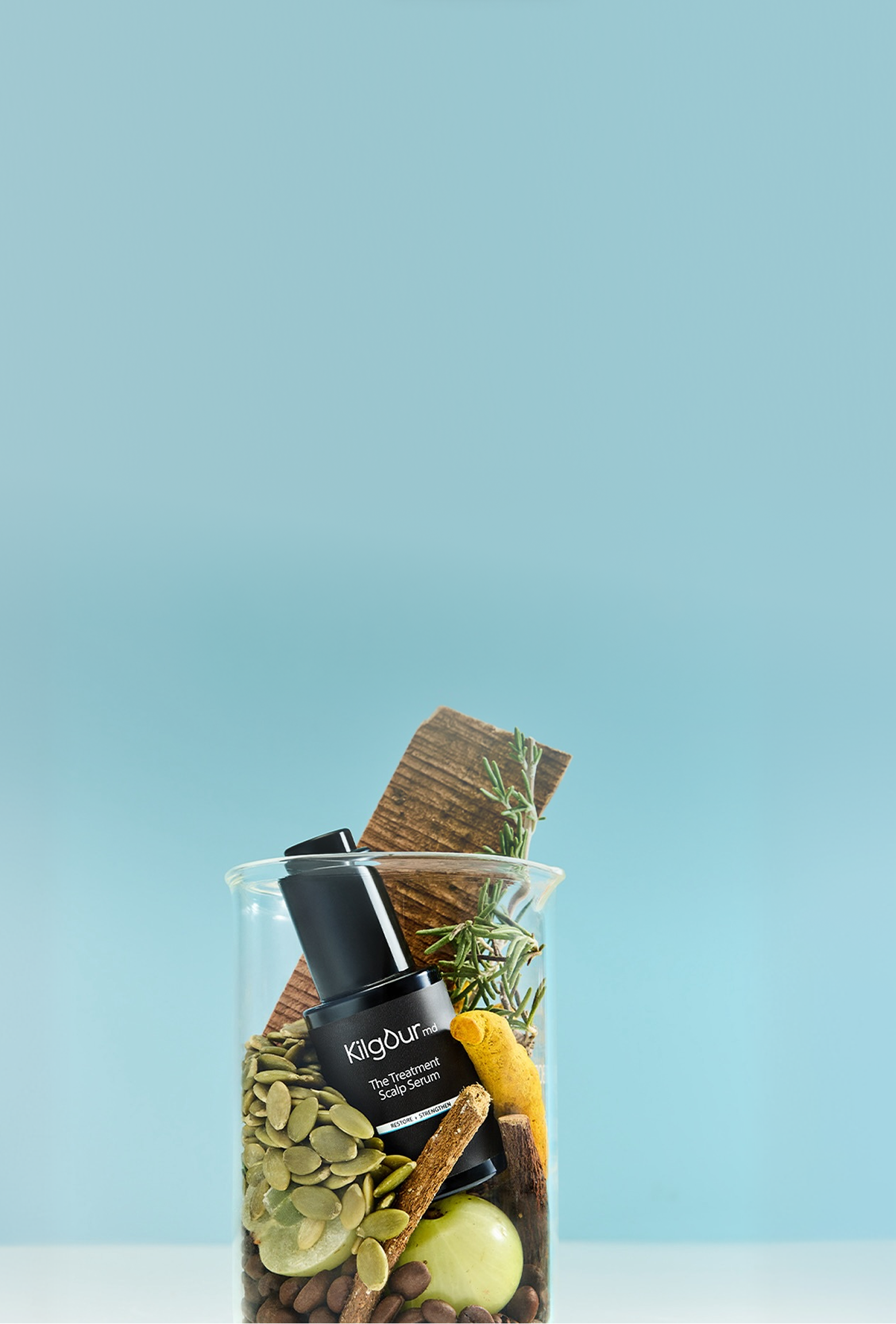 Angled view of KilgourMD The Treatment Scalp Serum, a black pump bottle among herbs, seeds, spices, and fruit