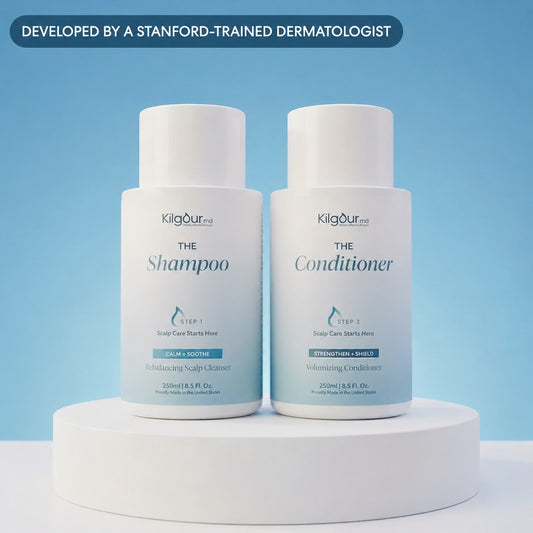 Front view of The Shampoo and Conditioner Bundle: two white KilgourMD bottles labeled The Shampoo and The Conditioner on a white pedestal against a light blue background with a ‘Developed by a Stanford-trained dermatologist’ banner